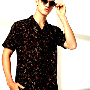 A male model wearing a black floral shirt with short sleeves, styled with white trousers and sunglasses.