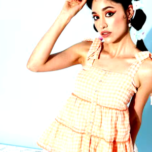 Woman wearing a peach gingham tiered sleeveless top with bow-tie shoulder straps.