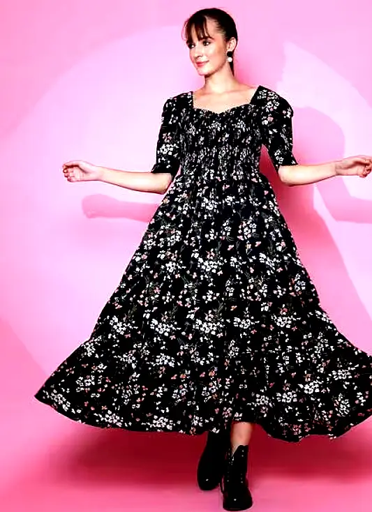 SHEETAL ASSOCIATES 5 Woman twirling in a black floral smocked maxi dress with puffed sleeves and a tiered hem.