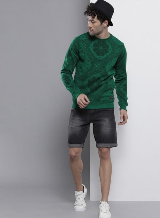 The Indian Garage Co 5 Man wearing a green sweatshirt with black shorts and white sneakers.