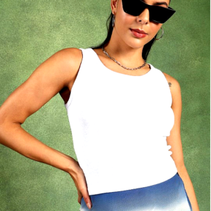 Woman wearing a white sleeveless ribbed tank top and blue gradient skirt, posing confidently with sunglasses against a green background.