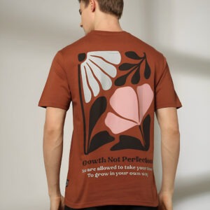 "A man wearing a brown short-sleeved T-shirt with a large abstract floral print and the quote 'Growth Not Perfection' on the back, paired with black pants."