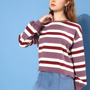 A fashionable young woman poses in a purple striped sweater and fitted denim jeans against a blue background, exuding a modern casual style.