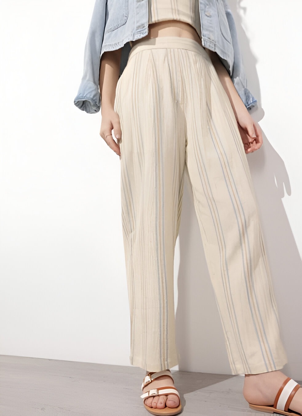 DressBerry 3 Woman wearing beige wide-leg pants with soft vertical stripes, paired with a cropped beige top, light-wash denim jacket, and brown strappy sandals, standing against a neutral background.