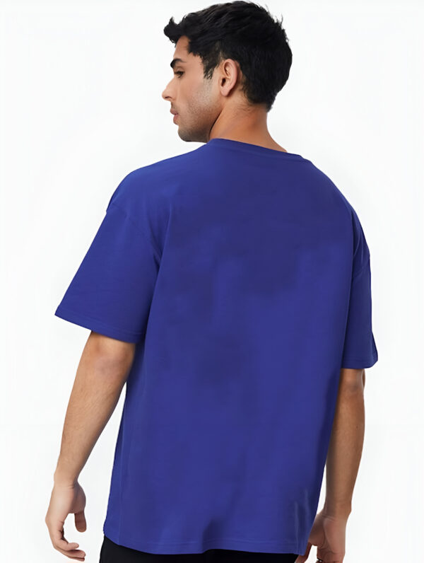 Back view of a man wearing a plain blue oversized T-shirt, standing against a white background.