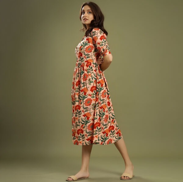 Woman wearing a floral midi dress with red and orange flowers, elbow-length sleeves, and beige open-toe sandals, posing against an olive-green background.