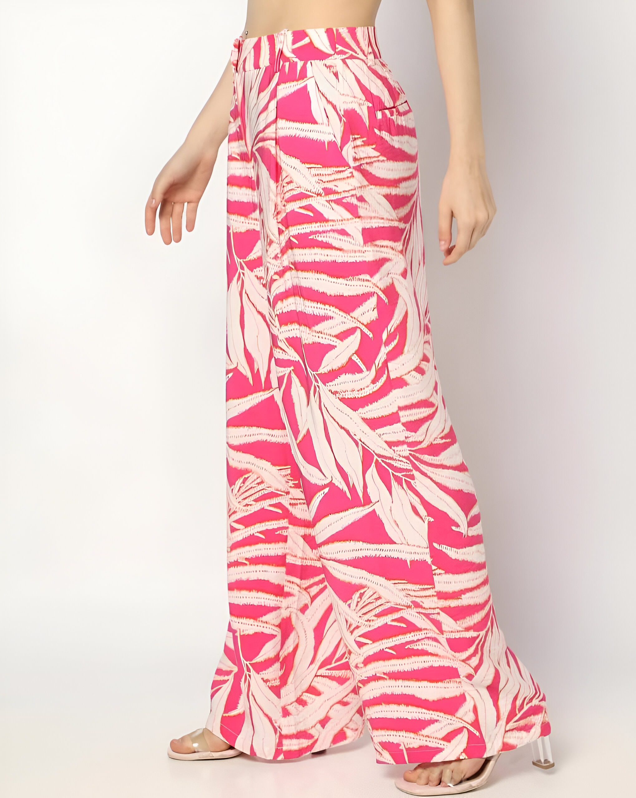 FIG 3 Side view of wide-leg tropical print pants with vibrant pink and white patterns, a high waist, belt loops, and paired with open-toe clear heels.