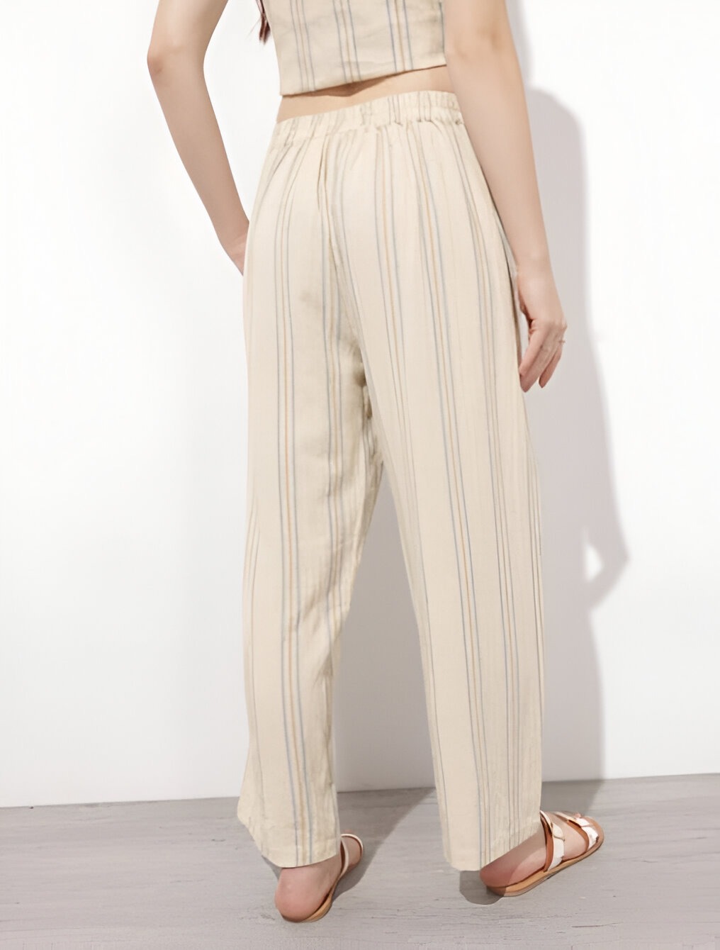 DressBerry 4 Back view of beige wide-leg pants with soft vertical stripes, elastic waistband, paired with a cropped beige top and brown strappy sandals against a neutral background.