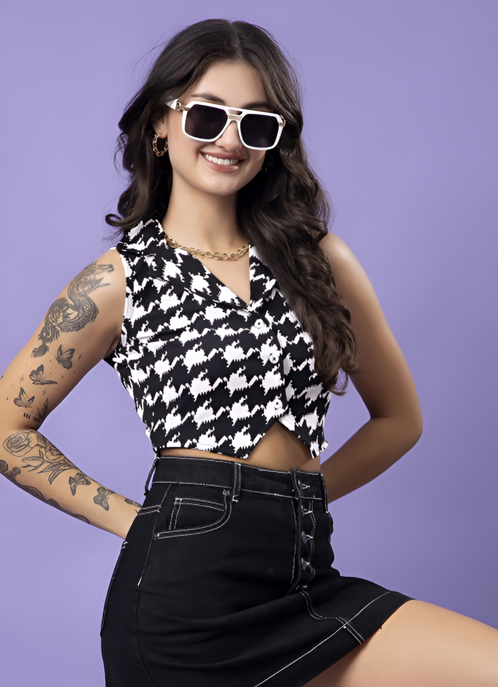  A trendy woman posing in a houndstooth cropped top paired with a black high-waisted skirt, accessorized with sunglasses and gold jewelry.