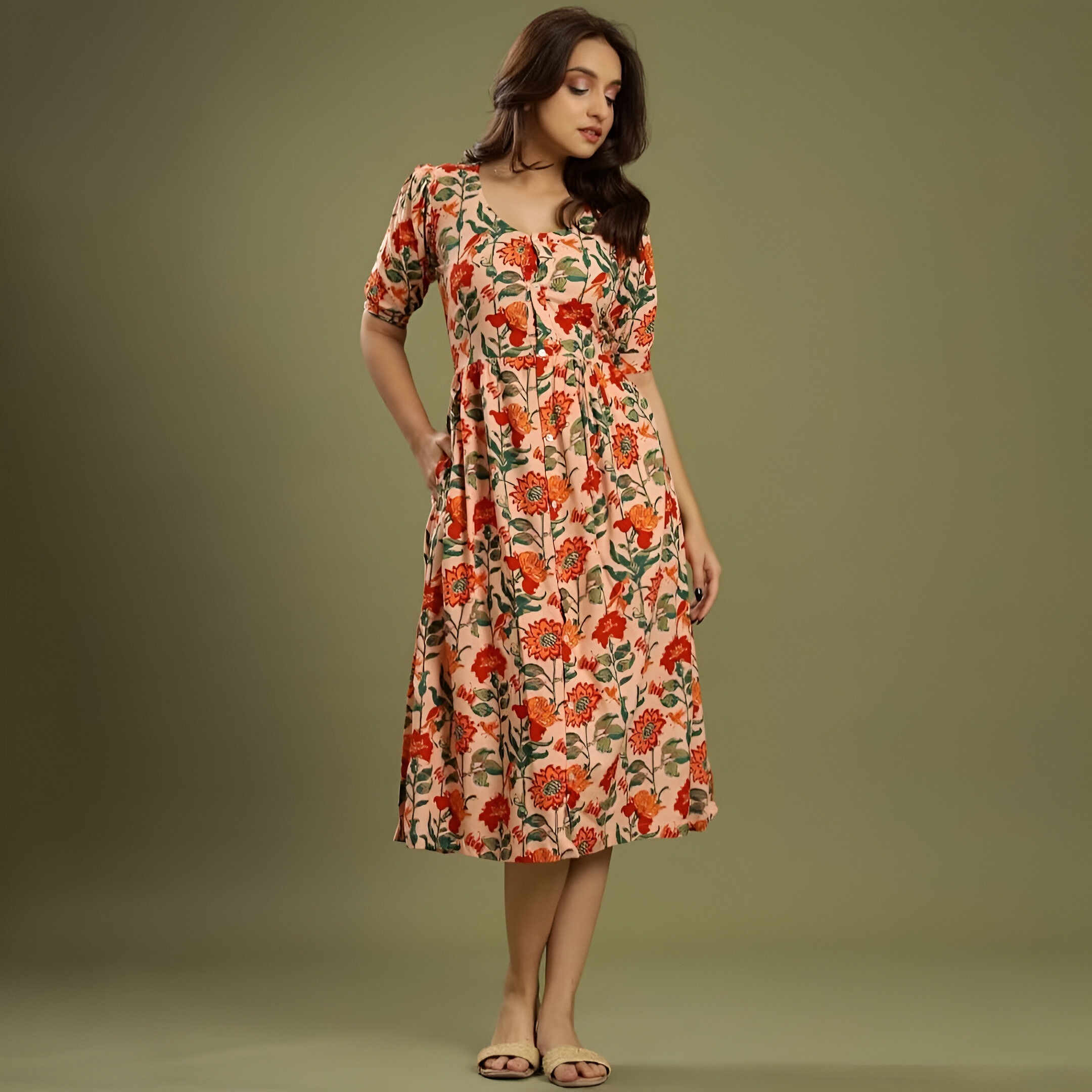 Negen 5 Woman wearing Negen floral midi dress with red and orange flowers, a cinched waist, elbow-length sleeves, and beige open-toe sandals, standing against an olive-green background.