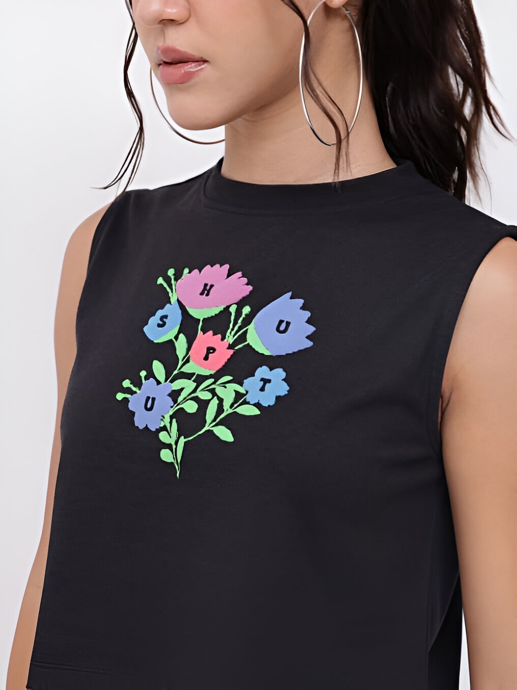 DressBerry 5 Close-up of a sleeveless dressberry black crop top with a colorful floral graphic print spelling "SHUT UP," paired with large silver hoop earrings.