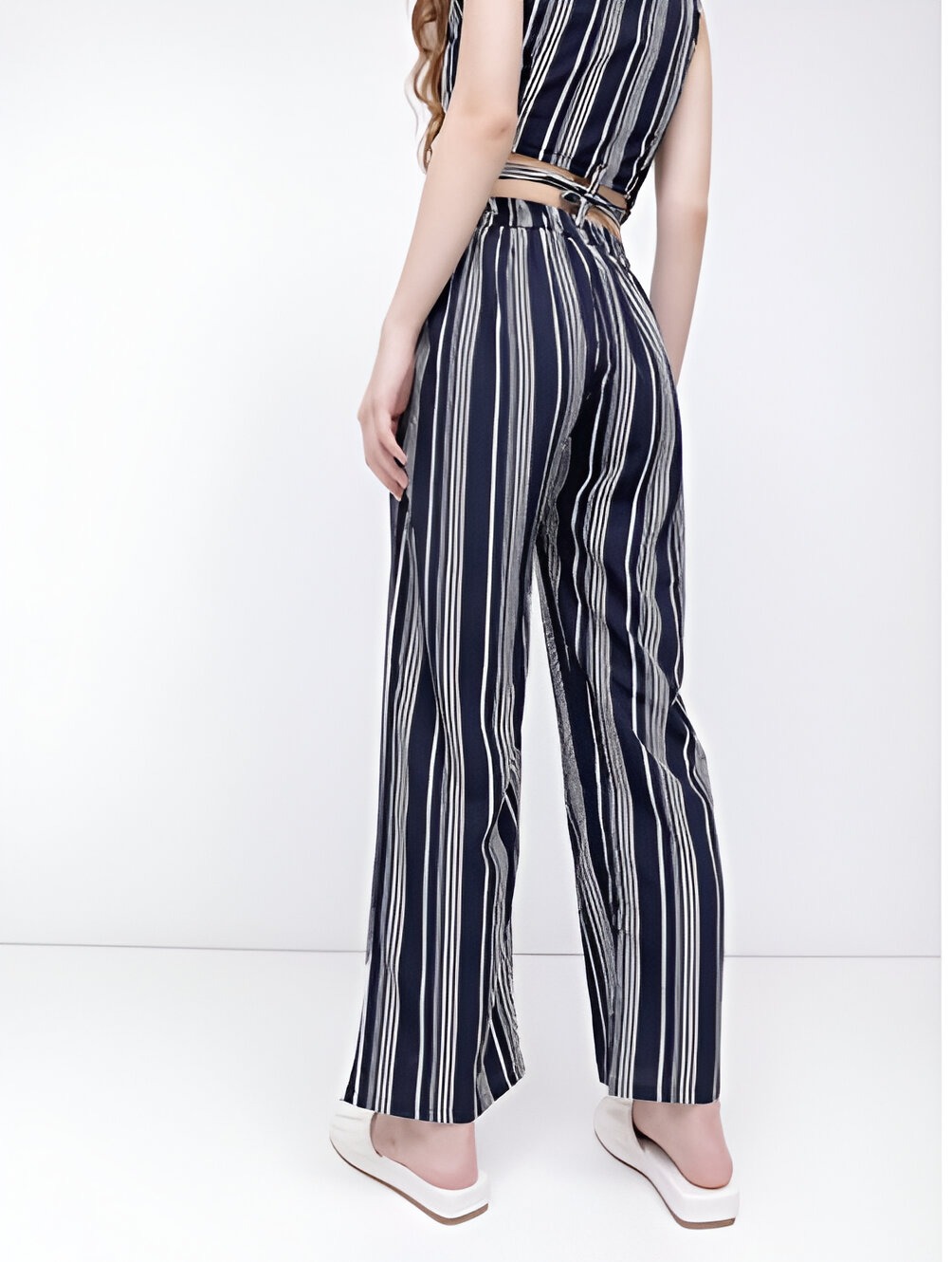 DressBerry 5 Back view of a woman wearing a navy blue and white striped co-ord set with a wrap crop top tied at the waist and high-waisted wide-leg trousers, paired with white platform sandals.