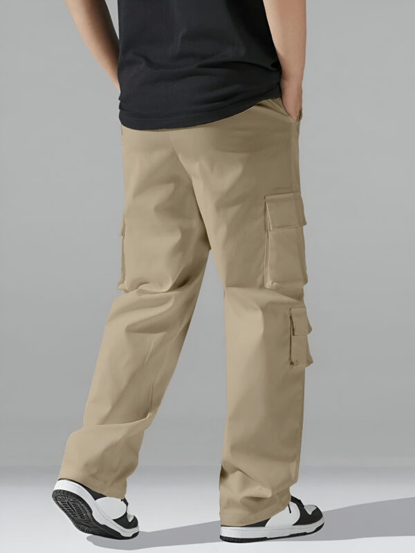 Back view of a person wearing beige cargo pants with large flap pockets and black and white sneakers, paired with a black T-shirt against a neutral gray background.