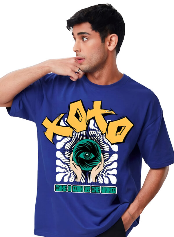 Man wearing a blue T-shirt with a large yellow graffiti-style "XOTO" text, an illustration of two hands holding a green eye-like sphere, and smaller text saying "Take a Look at the World."