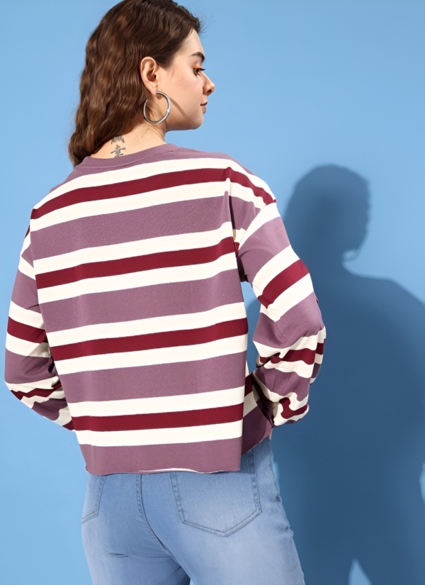 A young woman shows the back of a purple and white striped sweater paired with denim jeans, her wavy hair and tattoo adding a touch of personality.