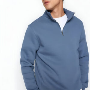 A man dressed in a blue quarter-zip pullover, white undershirt, and cap, standing against a plain white background.