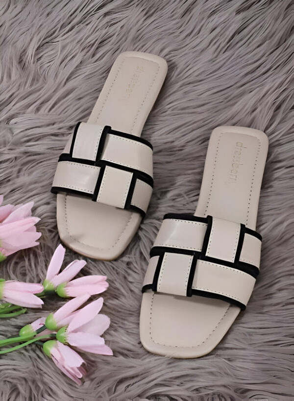 A pair of dressberry footwear beige slip-on sandals with black piping accents, displayed on a gray fur background with pink flowers beside them.